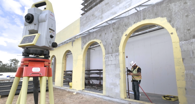 Construction worker in yellow vest and hard hat measures concrete layout position in an outdoor area using a Leica iCT30 layout tool.